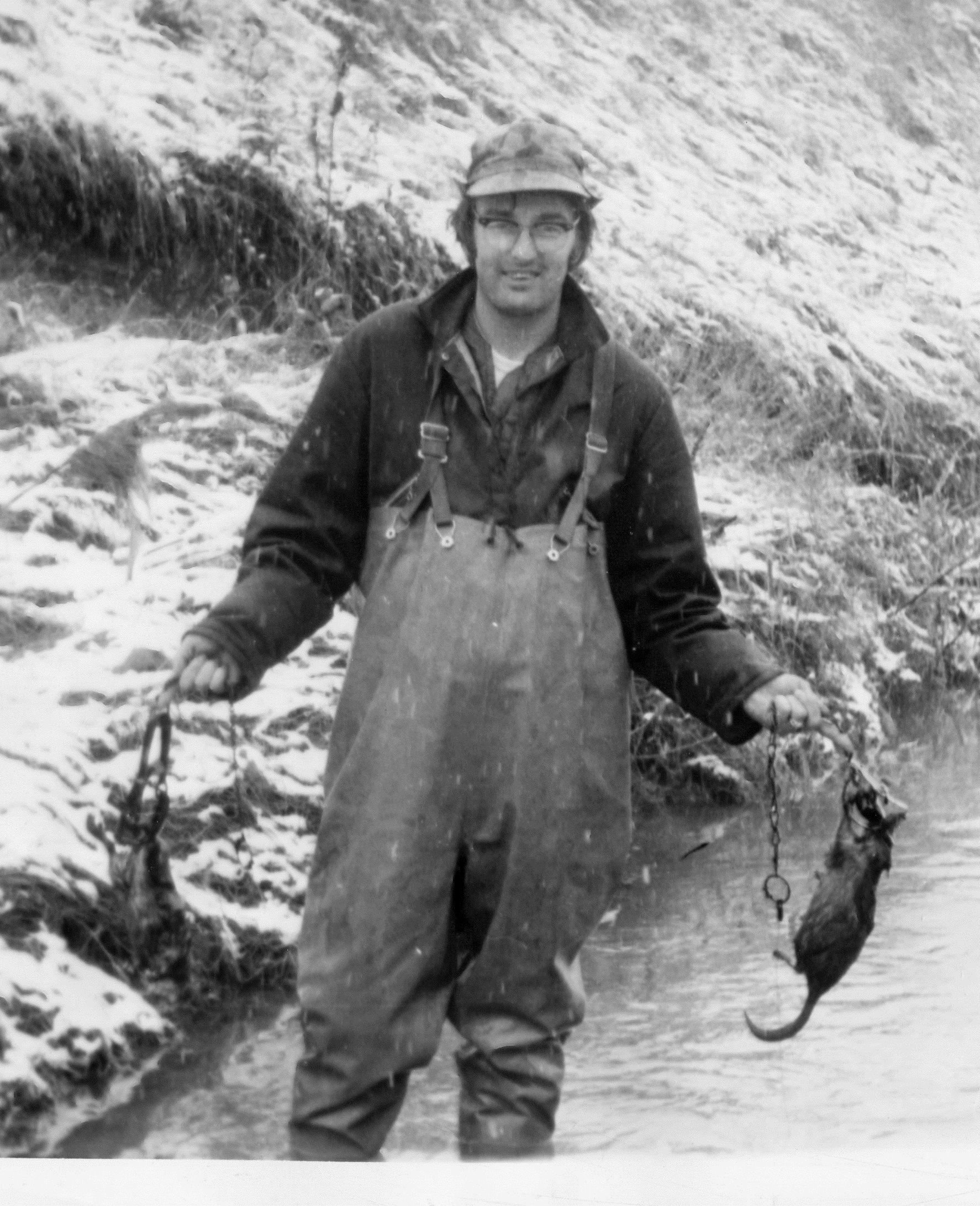A young man in 1968, standing in a stream while holding two muskrats in conibear traps