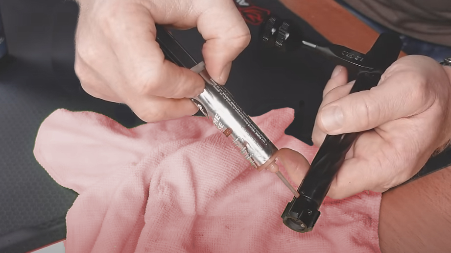 A macro shot of a single drop of oil being applied to a rifle's bolt lug